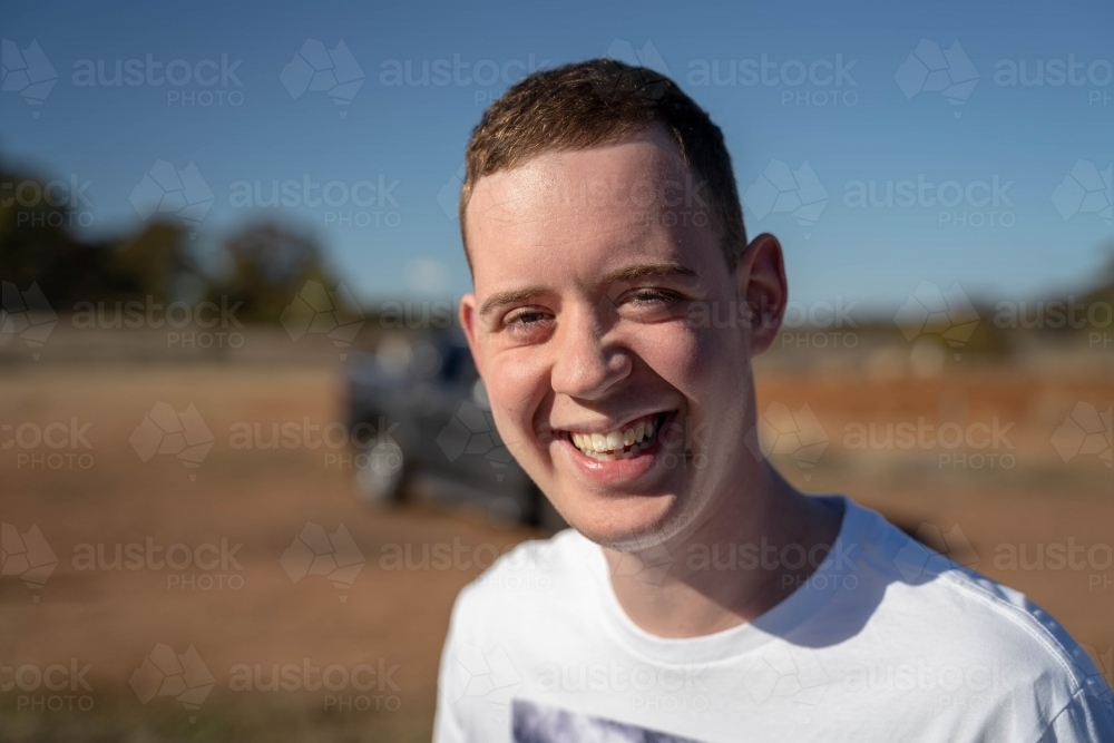 Young man standing outdoors under the sun smiling - Australian Stock Image
