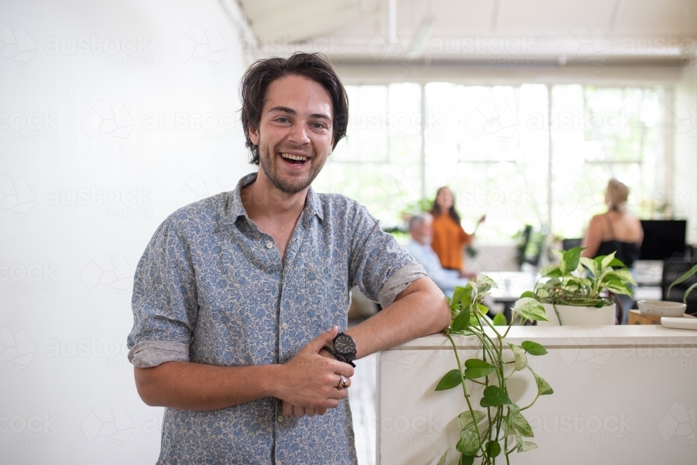 Young man standing, smiling in white office - Australian Stock Image
