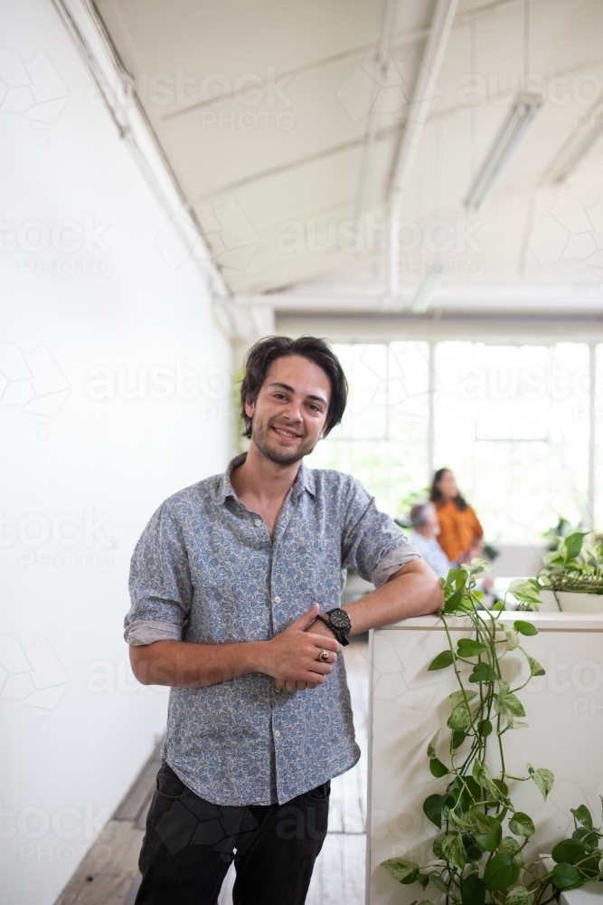 Young man standing, smiling in white office - Australian Stock Image
