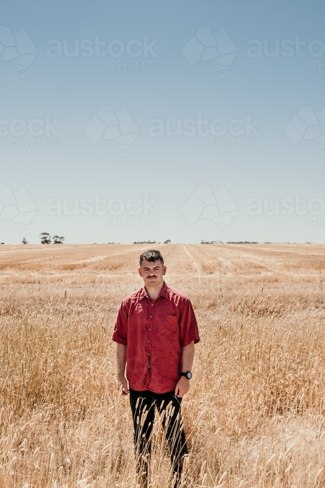 Young man stands in a dry paddock of grass. - Australian Stock Image