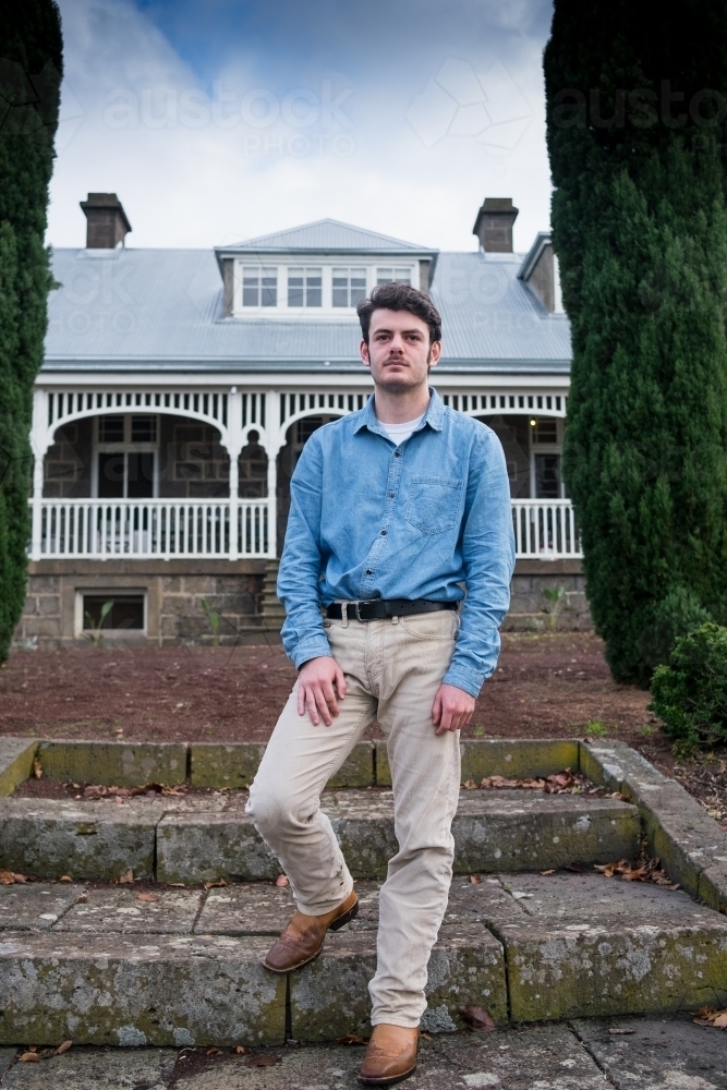 Young man stands in front of grand country homestead - Australian Stock Image