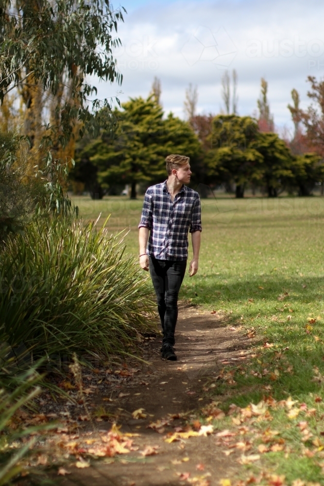 Young man walking alone along a path in nature : Austockphoto Young man walking alone along a path in nature - Australian Stock Image