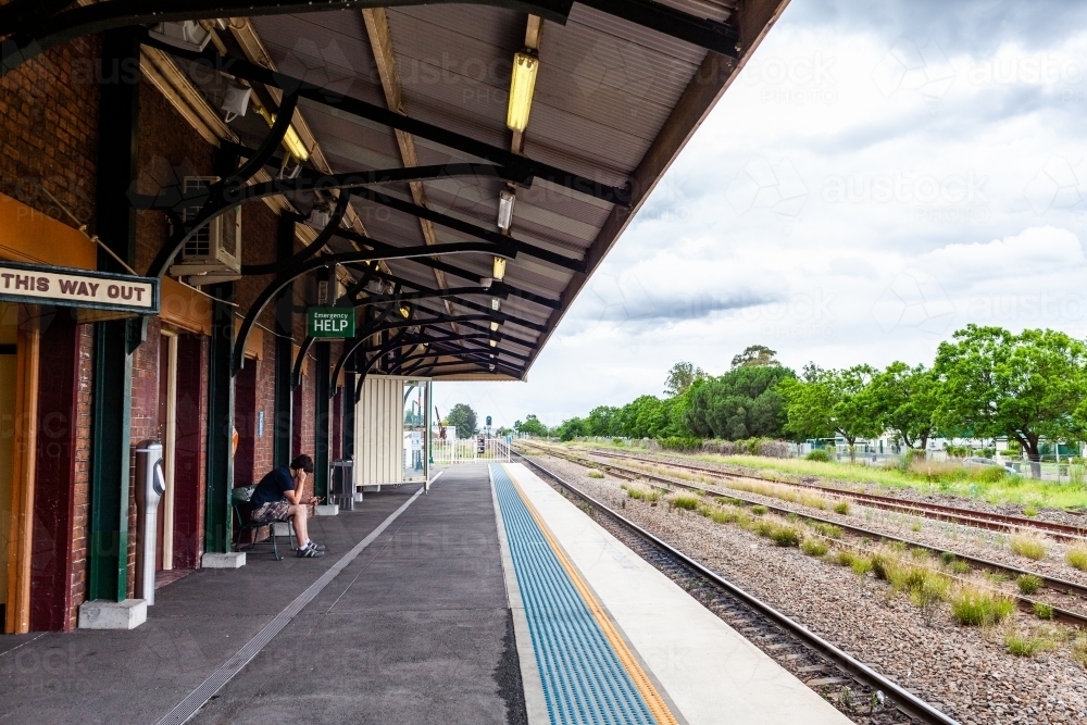 Young man wearing covid-19 face mask waiting at train station to travel to uni on public transport - Australian Stock Image