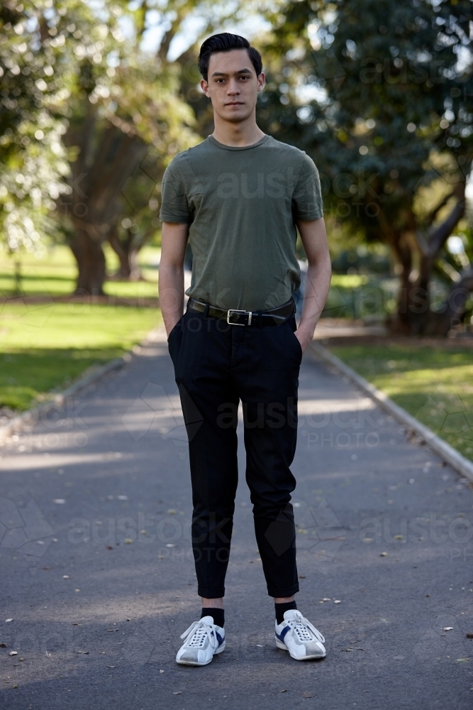 Young man with dark hair standing outside at park - Australian Stock Image