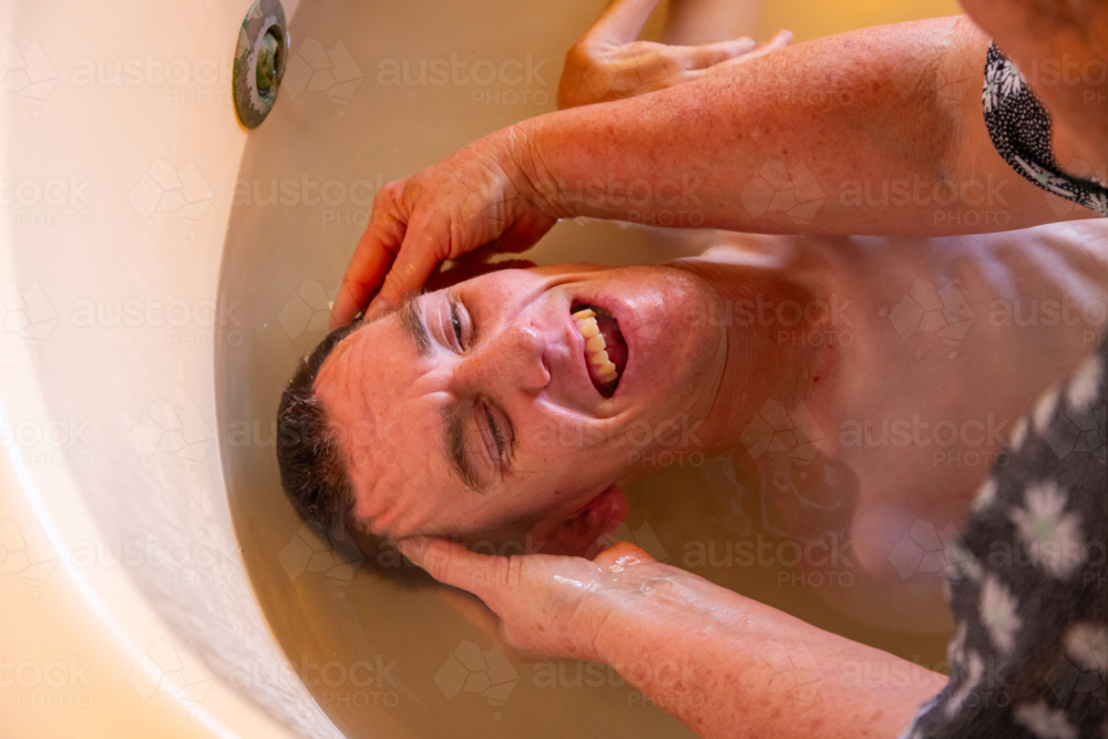 Young man with disability having a bath in a tub - Australian Stock Image