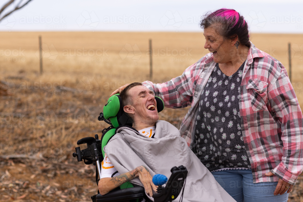 Young man with disability laughing with mother on dirt road in rural Australia - Australian Stock Image