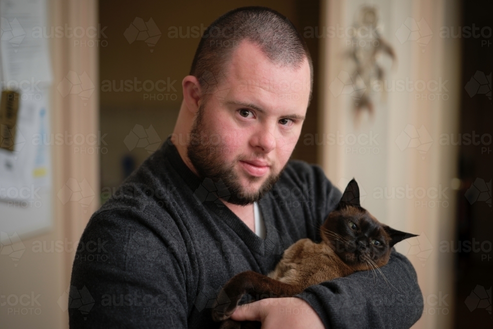 Young Man with Down Syndrome Cradling Cat - Australian Stock Image