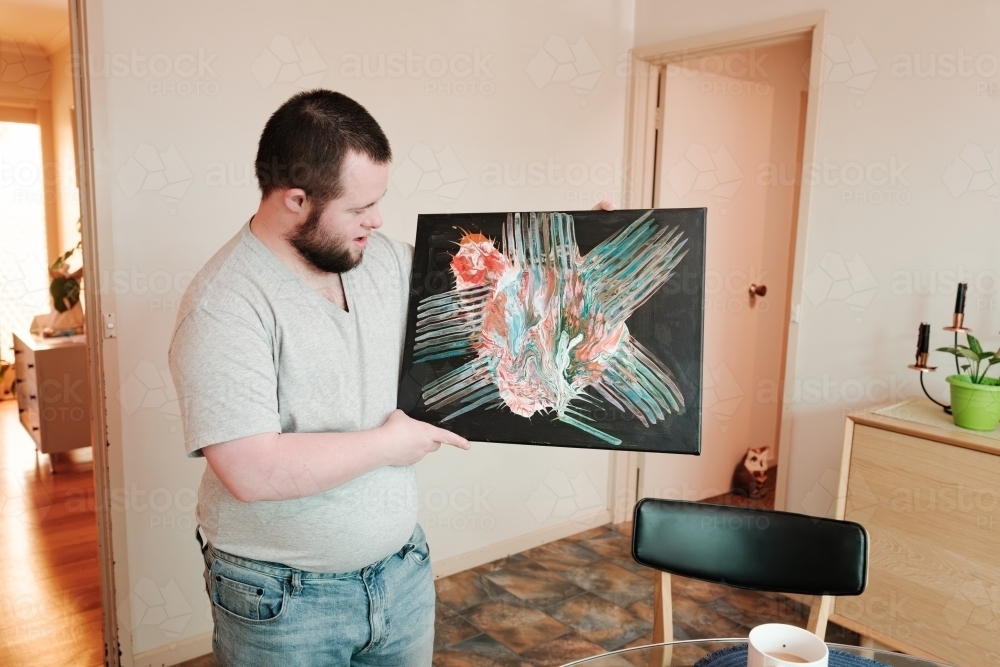 Young Man with Down Syndrome Proudly Holding His Painting - Australian Stock Image