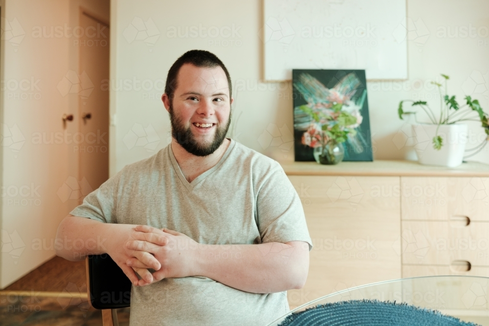 Young Man with Down Syndrome sitting on a chair smiling - Australian Stock Image