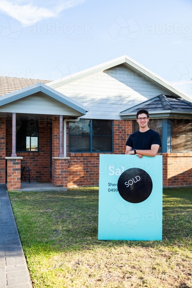 Image of Young man with sold sign and first home - Austockphoto