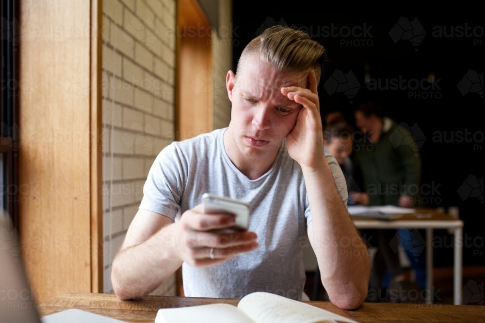 Young man with worried expression looking at his mobile phone - Australian Stock Image