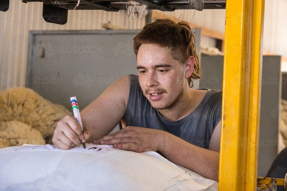 young man writing label on wool bale on farm - Australian Stock Image