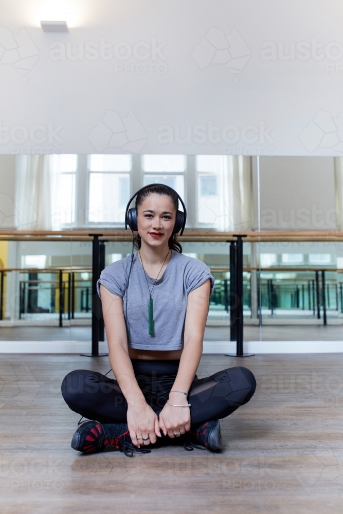 Young Maori woman seated listening to music in dance studio - Australian Stock Image