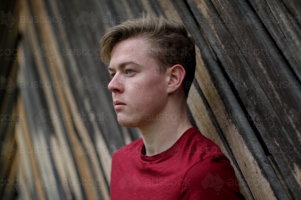 Young melancholy caucasian man modelling in front of a wooden panelled background - Australian Stock Image