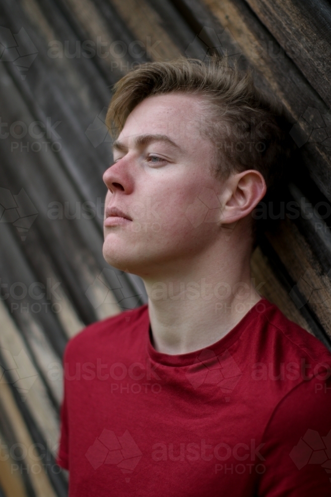 Young melancholy caucasian man modelling in front of a wooden panelled background - Australian Stock Image