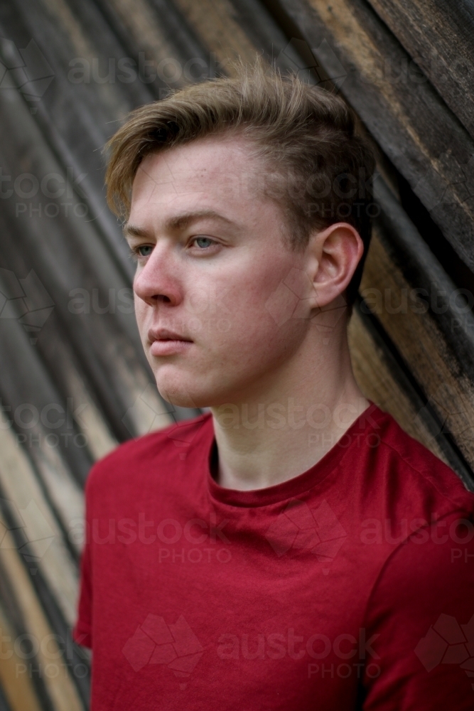 Young melancholy caucasian man modelling in front of a wooden panelled background - Australian Stock Image