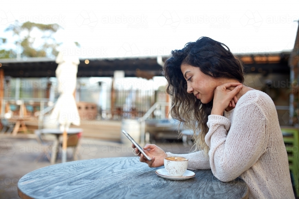 Young middle eastern woman enjoying time on phone at cafe - Australian Stock Image
