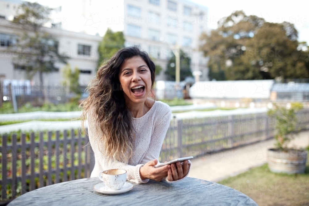 Young middle eastern woman enjoying time on phone at cafe - Australian Stock Image