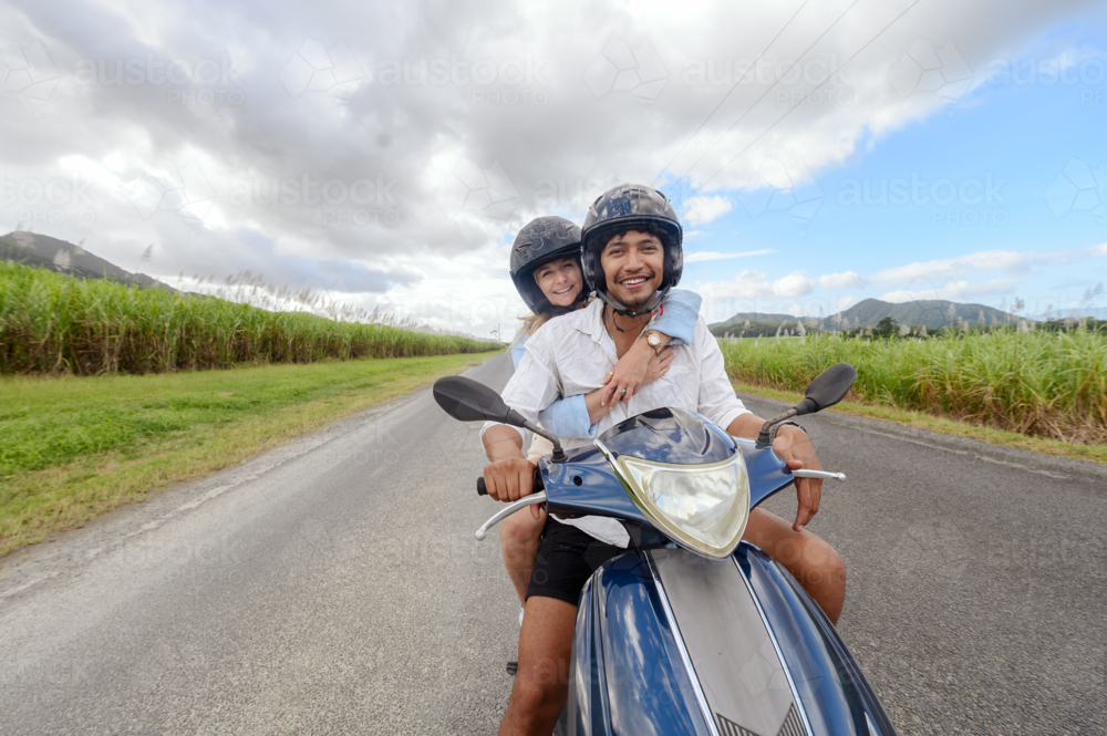 Young mixed race couple riding a motorbike together on a Queensland country road - Australian Stock Image