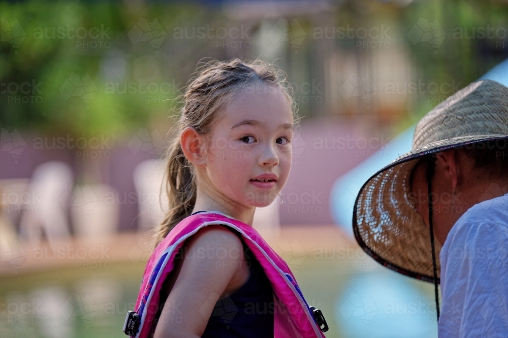 Young mixed race girl in swimming pool with vest on looking back over shoulder - Australian Stock Image