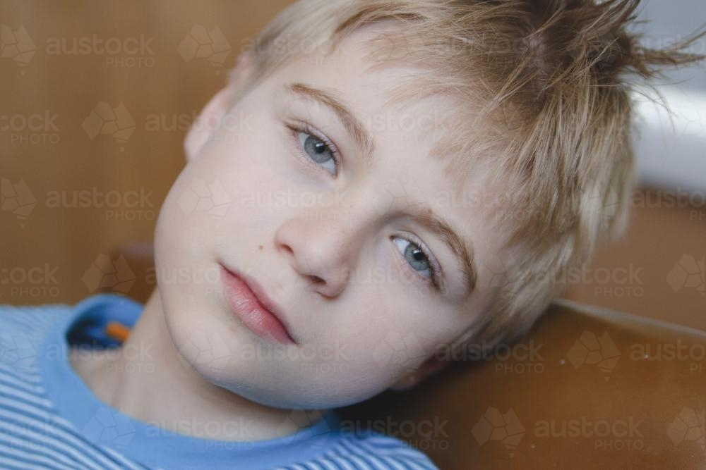 Young moody boy leaning on a leather couch - Australian Stock Image