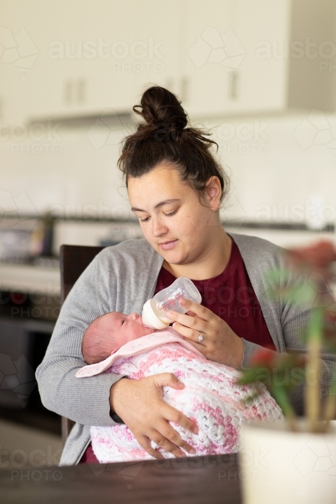 Young mother bottle-feeding baby girl at home - Australian Stock Image