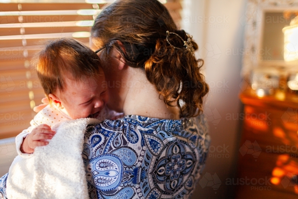 Young mother comforting sad crying baby child - Australian Stock Image