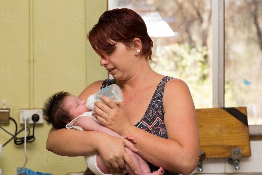 Young mother feeding infant with formula in a bottle - Australian Stock Image
