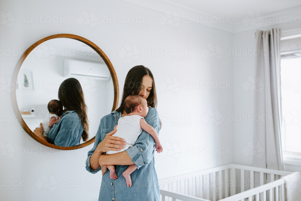 Young mother holding newborn baby boy in front of mirror - Australian Stock Image