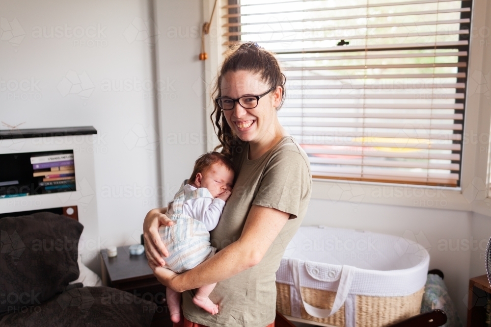 Young mother holding newborn baby in bedroom in home - Australian Stock Image