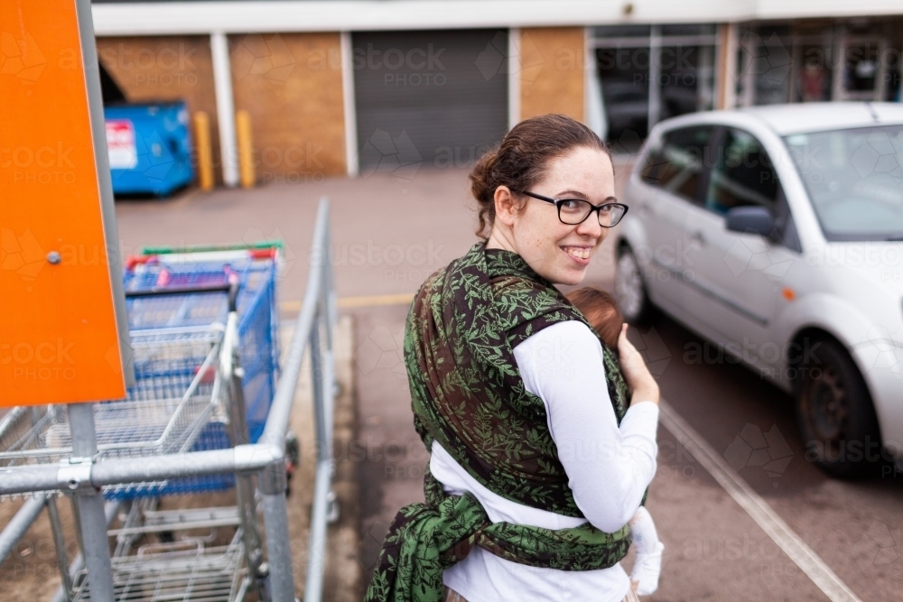 Young mum carrying baby through carpark out and about - Australian Stock Image