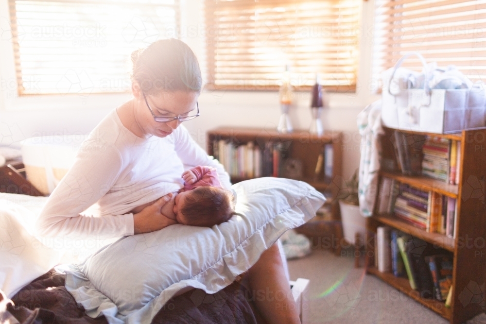 Young mum in bedroom breastfeeding content newborn baby with light flare - Australian Stock Image