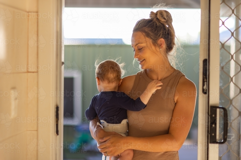 young mum in doorway holding baby wearing hip brace for hip dysplasia - Australian Stock Image