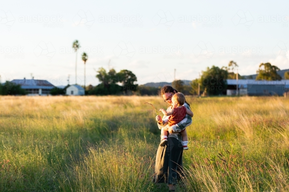 Young mum with toddler in rural country setting going for walk in farm paddock on autumn afternoon - Australian Stock Image