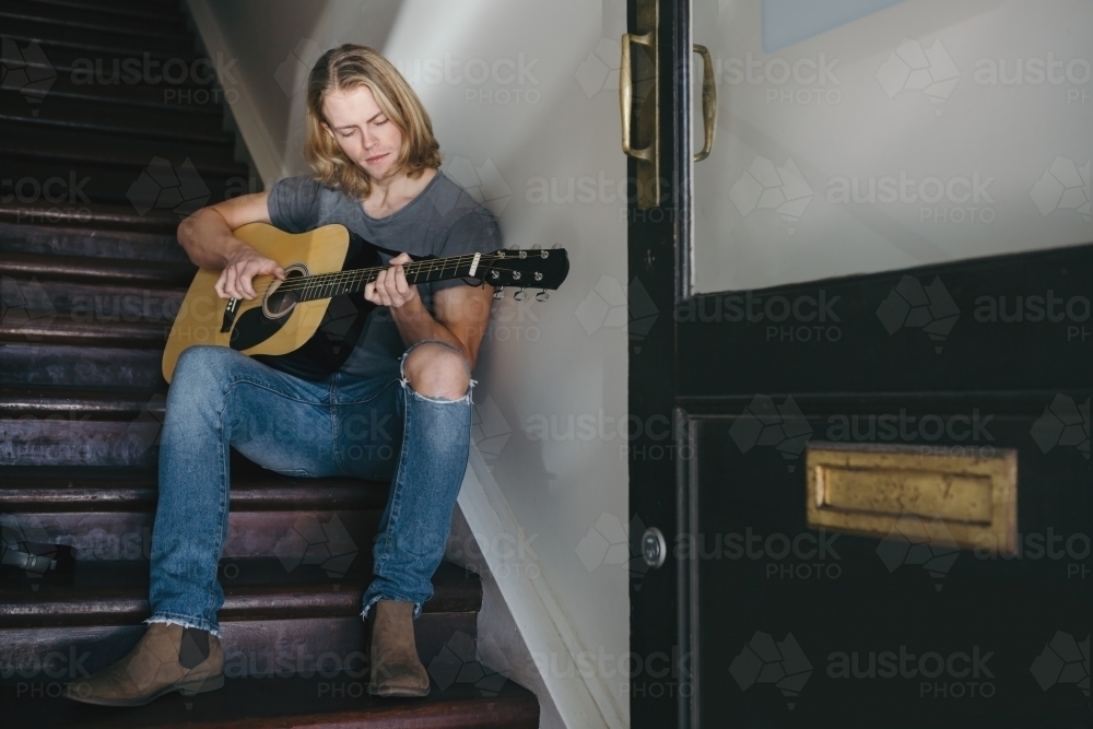 Young musician playing guitar on the stairs - Australian Stock Image