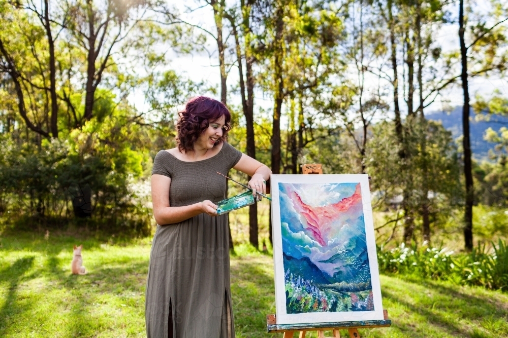 Young nineteen year old artist hobbyist with her painting standing outside in clearing - Australian Stock Image