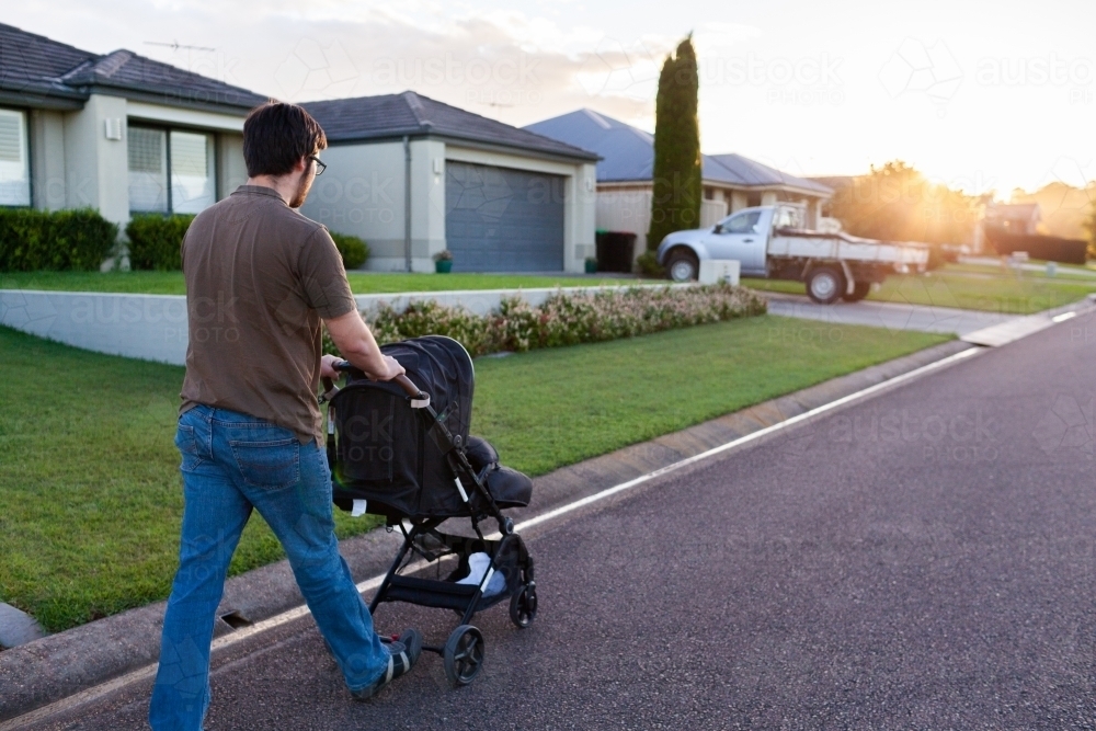 Young parent pushing baby in pram down road at sunset - Australian Stock Image
