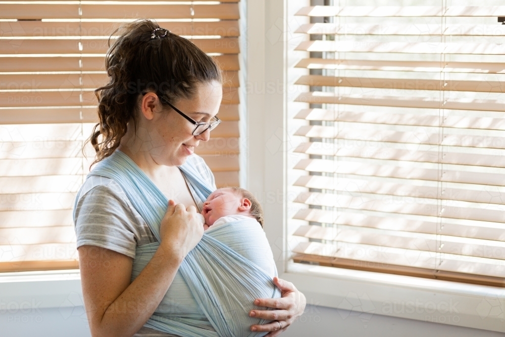 Young parent with sleeping newborn infant babywearing in wrap sling - Australian Stock Image