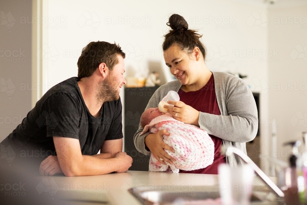 Young parents in kitchen feeding newborn baby girl - Australian Stock Image
