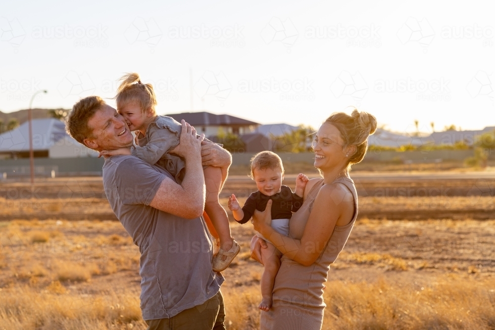 young parents with two young kids in golden light with houses in background - Australian Stock Image