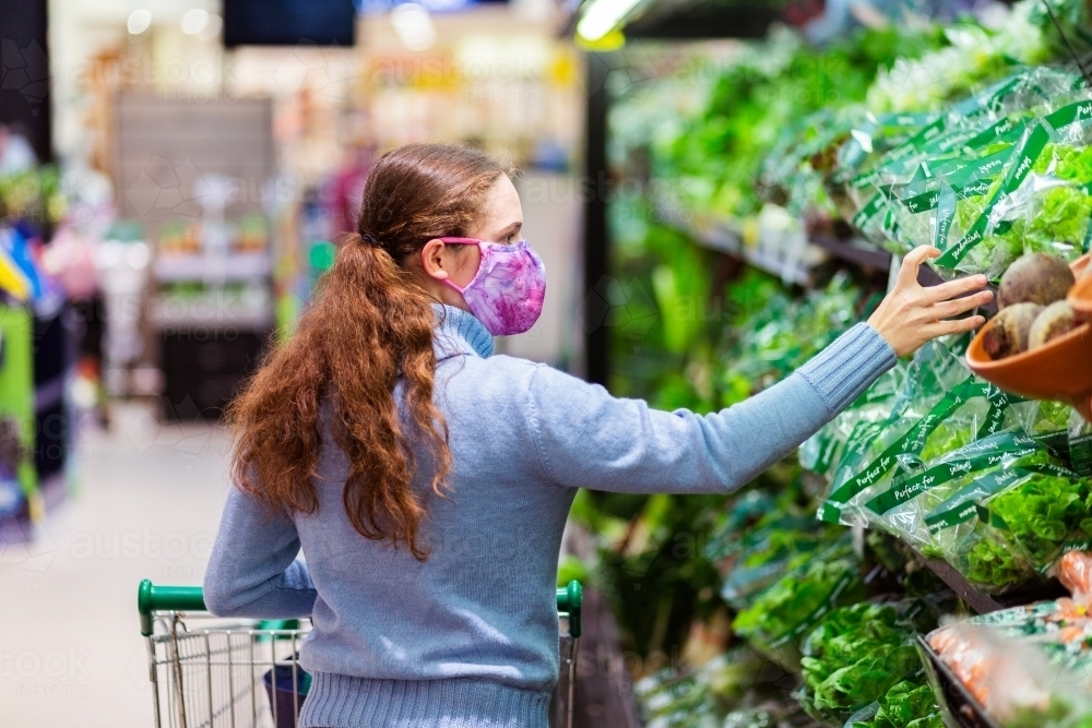 Young person doing grocery shopping during the covid-19 pandemic picking lettuce off the shelf - Australian Stock Image