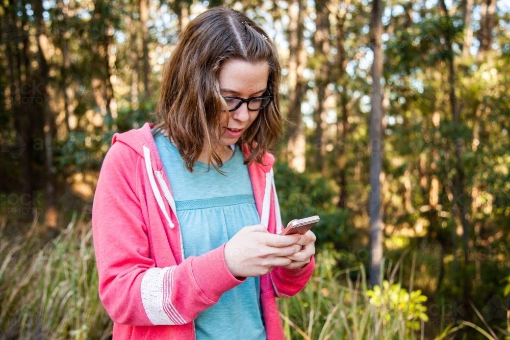 Young person holding mobile phone texting in forest - Australian Stock Image