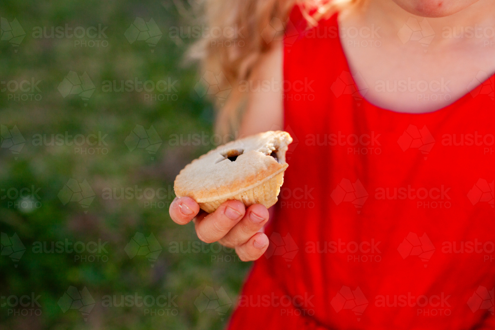 Young person in red for christmas enjoying Christmastime fruit mince pie in Australian backyard - Australian Stock Image