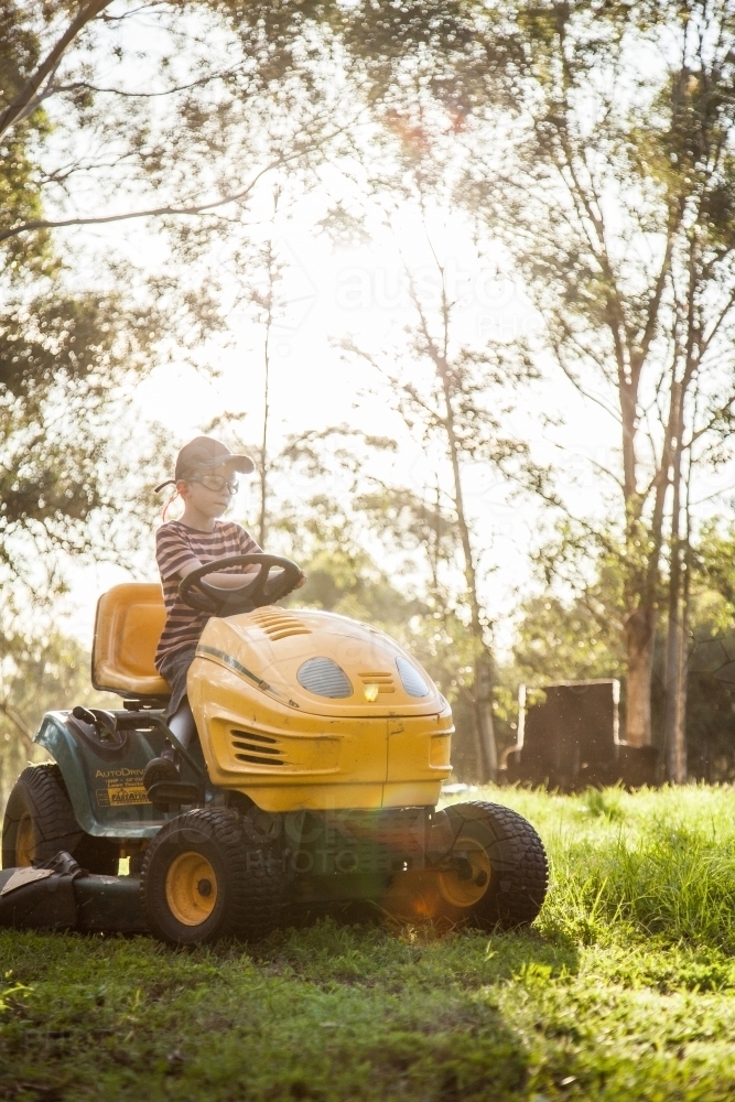 Young person mowing the paddock on a ride on lawn mower in afternoon sunlight - Australian Stock Image
