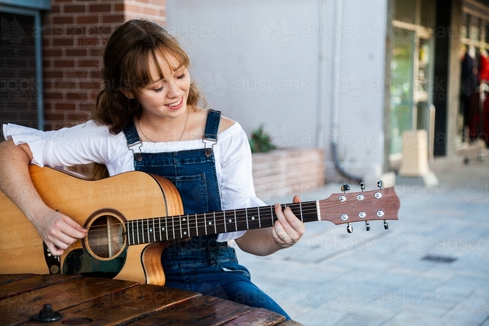 Young person playing guitar outside cafe - Australian Stock Image