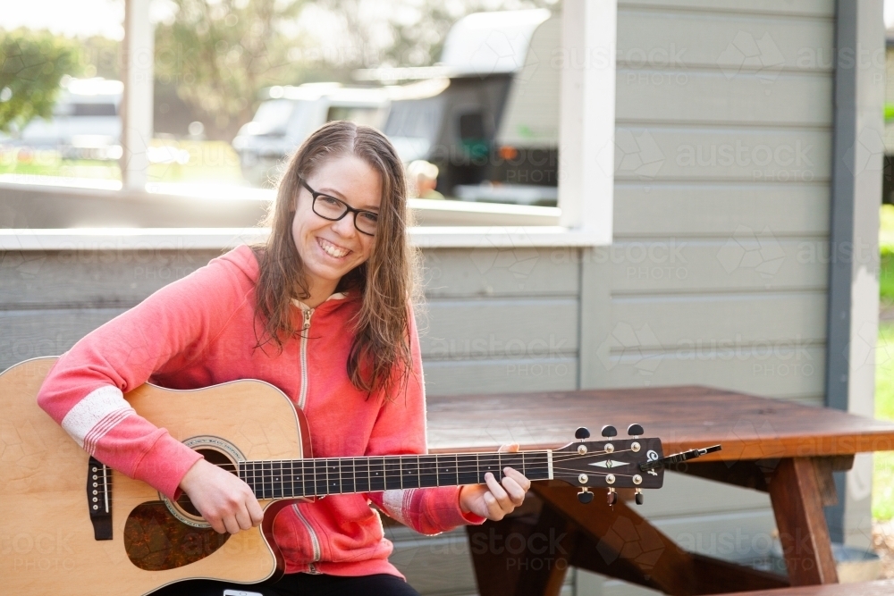 Young person playing guitar outside sitting on park bench - Australian Stock Image