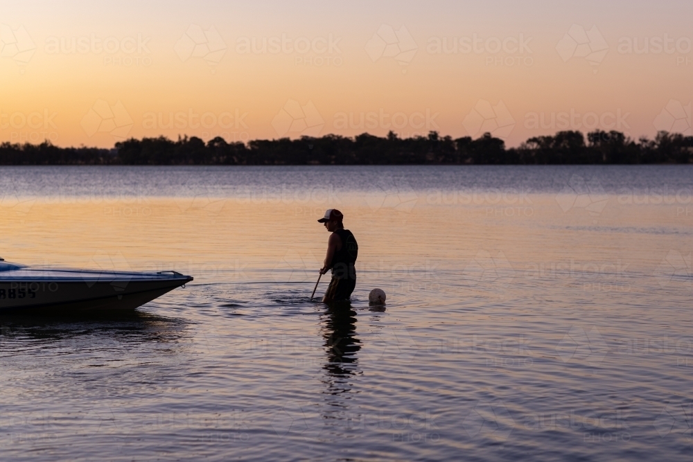young person pulling up anchor of speedboat on lake - Australian Stock Image