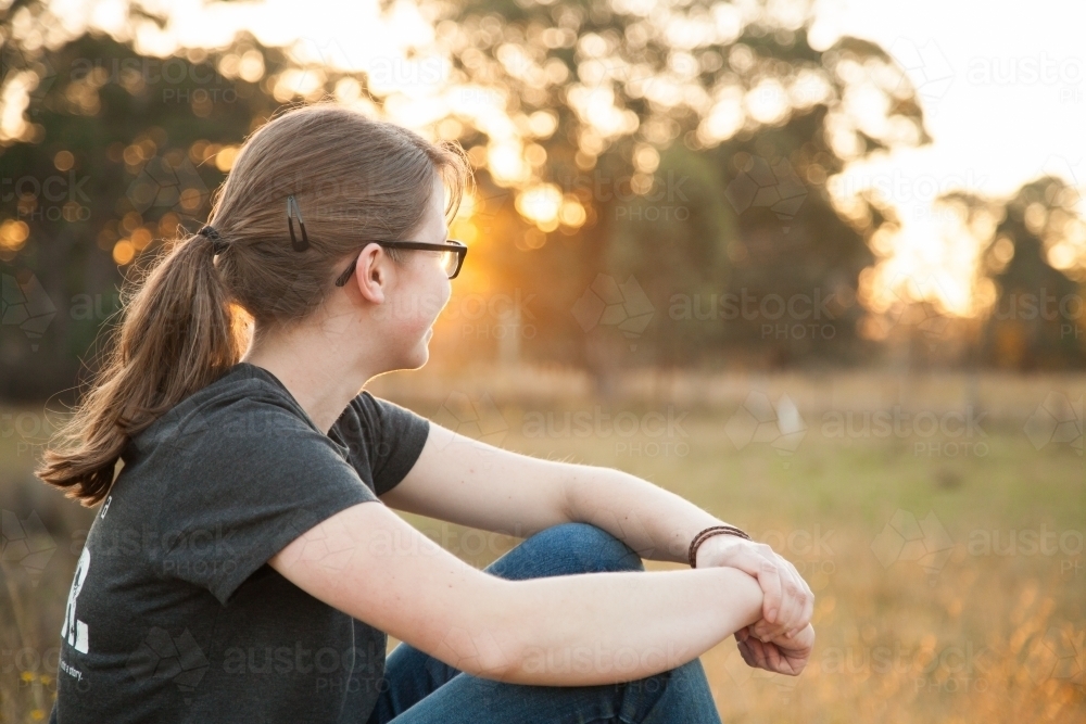Young person sitting outside at sunset looking away - Australian Stock Image