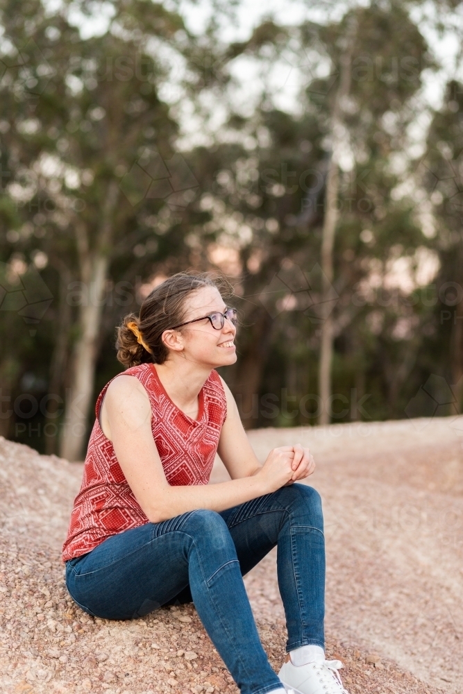 Young person sitting outside on dirt heap at dusk with bokeh light - Australian Stock Image