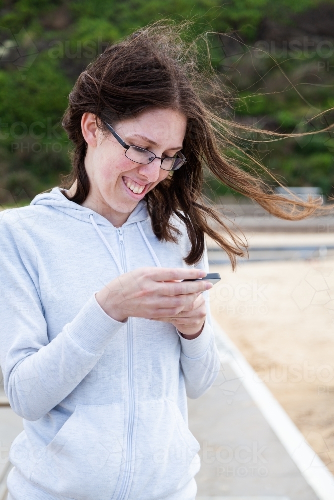 Young person using her mobile phone at the beach on windy day - Australian Stock Image